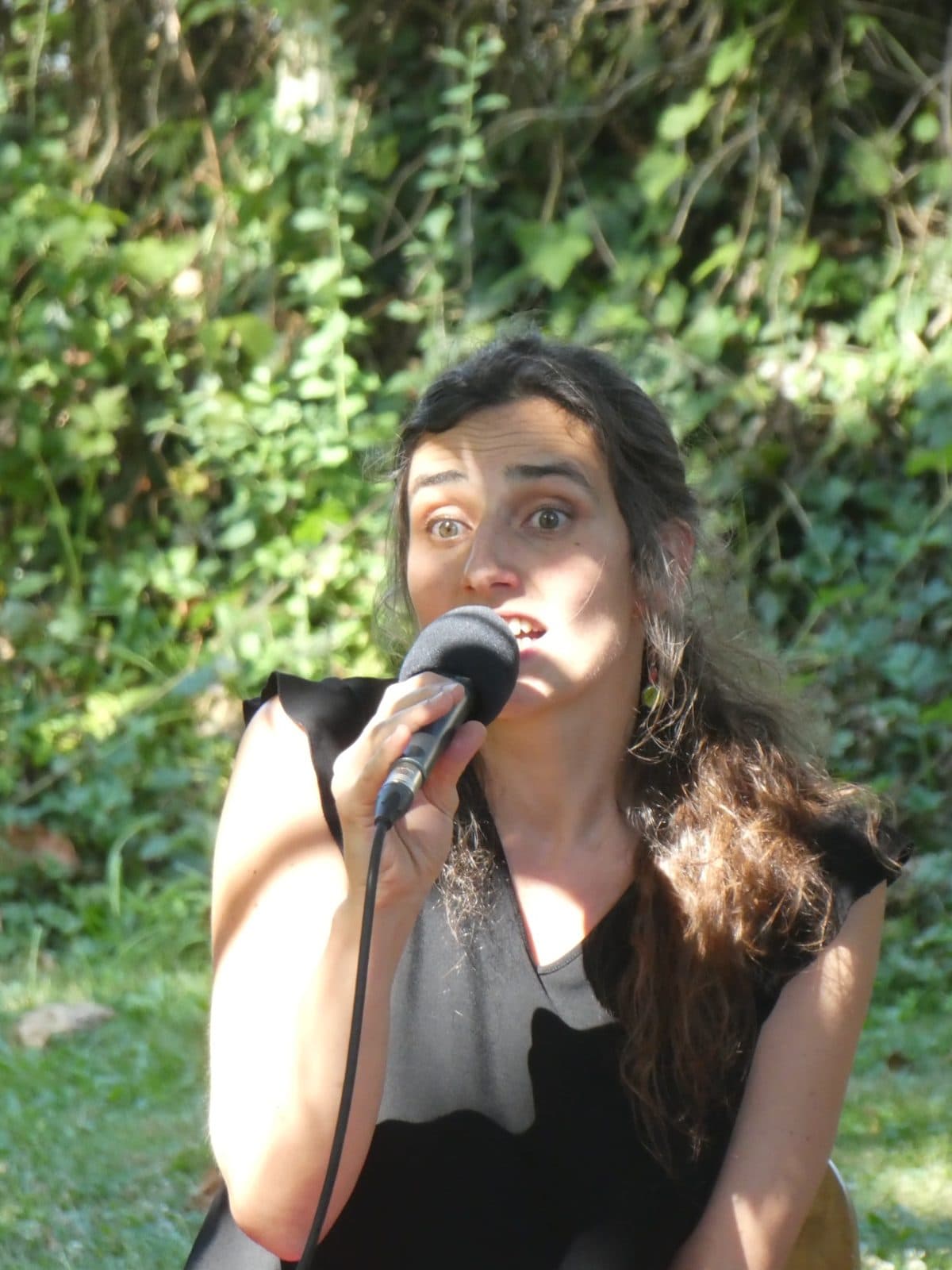 La chanteuse du Trio Volubile, micro à la main, devant le feuillage du parc