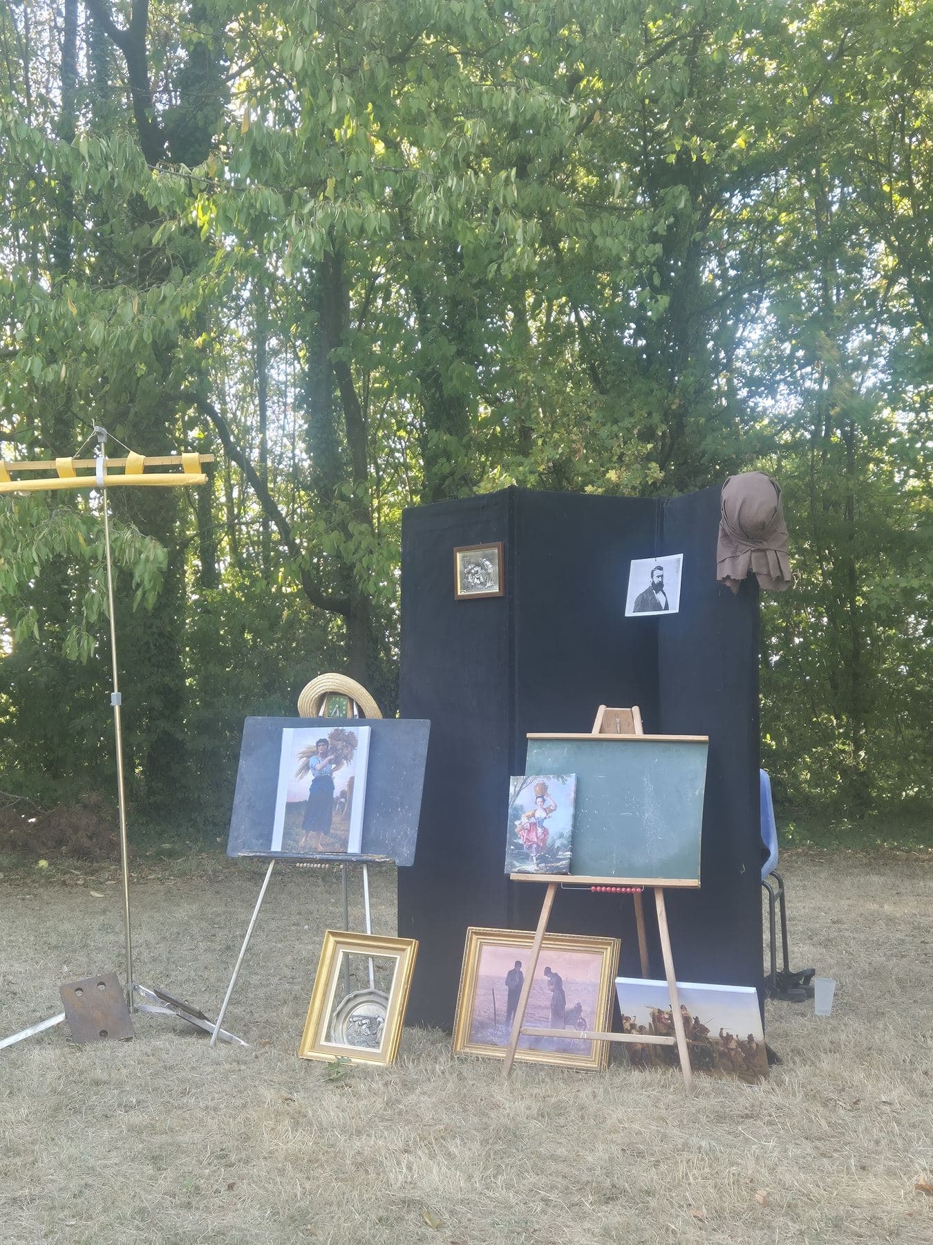 Le décor de la conférence : un paravent noir, des chevalets et des reproductions de tableaux de Millet posées dans l’herbe